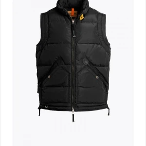 Svart dunväst med dragkedja Parajumper - Snygg svart dunväst med dragkedja och hög krage. Västen har praktiska fickor med knappar och en gul detalj vid kragen. Perfekt för våren/hösten. Köpt på NK för 5000