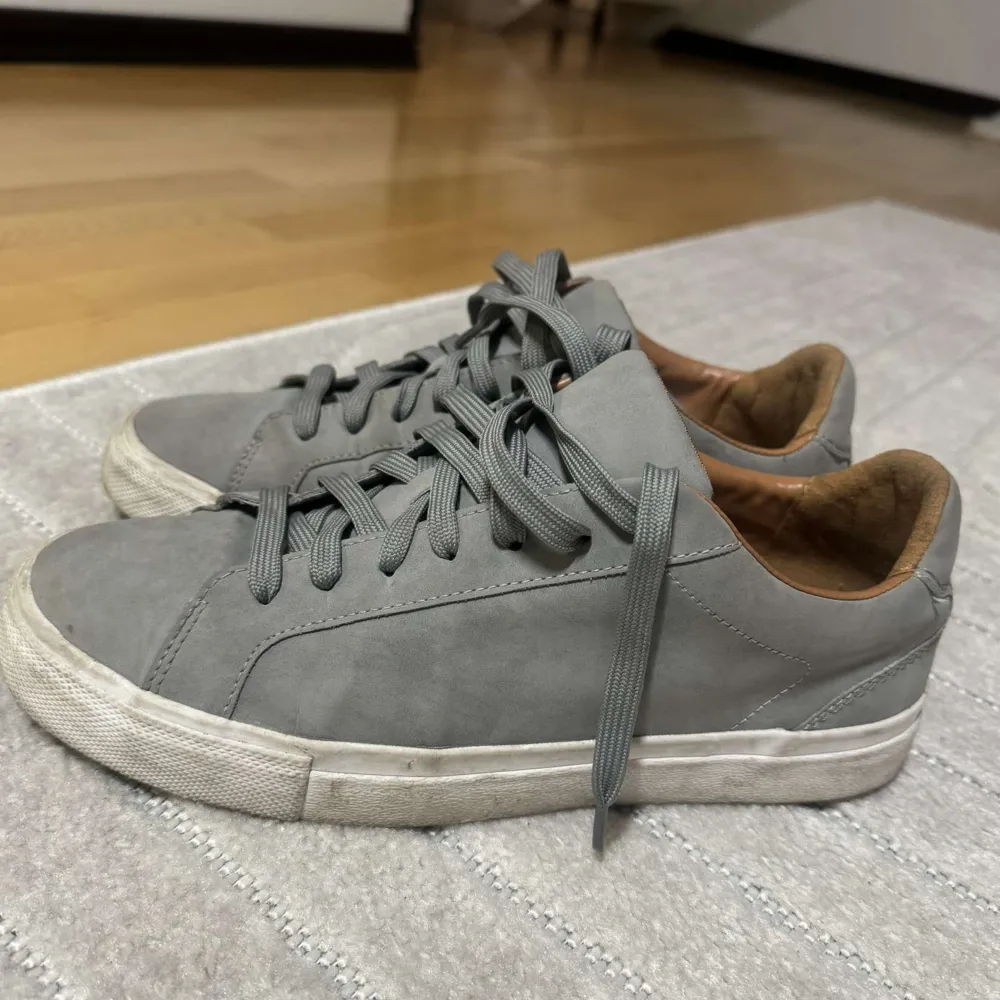 Snygga grå sneakers med snörning och rund tå. Perfekta för en avslappnad stil. Skorna har en vit sula och är tillverkade i ett syntetmaterial.. Kengät.