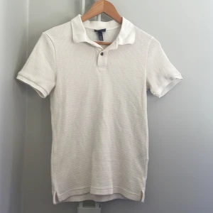 Vit pikétröja från H&M - Snygg vit pikétröja från H&M med korta ärmar och klassisk krage. 