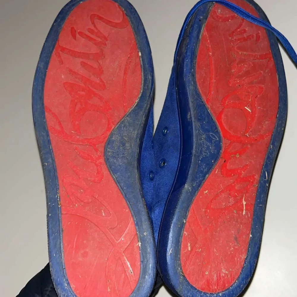 Snygga blå sneakers från Christian Louboutin med ikoniska röda sulor och nitar på tån. Skorna har snörning och en unik design som sticker ut. Perfekta för den som vill ha något extra i sin skogarderob.. Kengät.