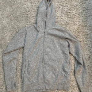 Grå hoodie med dragkedja - Säljer en stilren grå hoodie med dragkedja. Perfekt för en avslappnad look. Den har långa ärmar och en praktisk huva. Passar bra till både jeans och träningsbyxor.