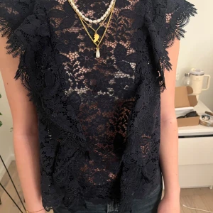 Marinblå spetsblus - Snygg svart spetsblus med korta ärmar och vackra spetsdetaljer. Perfekt för en elegant look med ett genombrutet mönster som ger en feminin touch. Passar bra med smycken för att lyfta outfiten.