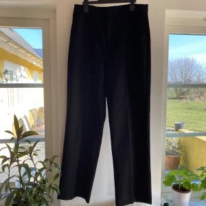 Svarta byxor från Gina Tricot - Snygga svarta byxor från Gina Tricot med dragkedja och knapp framtill. Byxorna har en klassisk rak passform och är perfekta för en stilren look. Tillverkade i ett bekvämt material som passar till många olika tillfällen. Små i storleken.