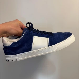 Blåa Valentino Flycrews  - Snygga blå sneakers i mocka från Valentino med vita detaljer och silverfärgade nitar på hälen. Skorna har en klassisk snörning och en vit sula som ger en stilren look. (NYSKICK) (ALLA NITAR KVAR)