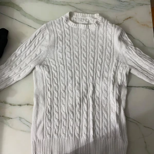 Vit stickad tröja från 157 - Säljer en stilren vit stickad tröja från 157 med klassiskt flätmönster. Tröjan har långa ärmar och en rund halsringning, perfekt för kyligare dagar. Passar bra till både jeans och kjol.