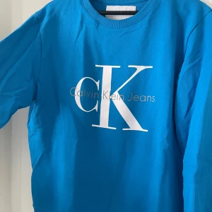 Blå tröja från Calvin Klein  - Säljer en snygg blå tröja från Calvin Klein Jeans med deras ikoniska logga tryckt på framsidan. Tröjan har långa ärmar och en rund halsringning. Perfekt för en stilren och avslappnad look. Nypris 1199kr.