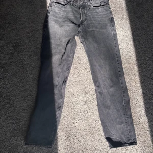 Grå jeansbyxor med rak passform - Snygga grå jeansbyxor från H&M med original straight fit. Perfekta för en avslappnad stil, dessa byxor har en klassisk design med fem fickor och knappgylf. Tillverkade i Bangladesh.