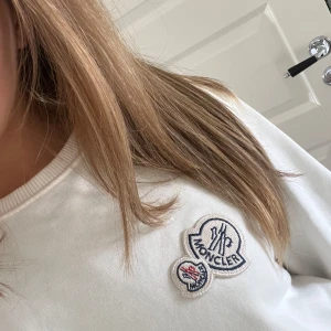 Vit sweatshirt från Moncler - Säljer en mysig oversized vit sweatshirt från Moncler med deras ikoniska logga på bröstet. Tröjan har långa ärmar och ribbade muddar vid ärmslut och nederkant. Perfekt för en avslappnad look. (Köpt second hand vet ej om den är äkta) priset går att pruta.