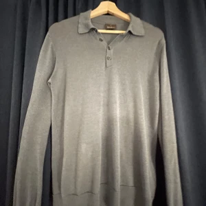 Grå pikétröja från Oscar Jacobson - Snygg och stilren grå pikétröja från Oscar Jacobson. Tröjan har långa ärmar och en klassisk krage med knappar framtill. Perfekt för en elegant och avslappnad look. Skicket är bra!  // Svéd Resell 