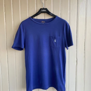 Ralph Lauren T-shirt med ficka  - En fin Ralph Lauren t-shirt i mycket bra skick. Längden är: Axelbredd:45 Längd:70  Nypriset ligger på ca 700kr som du kan se på sista bilden.   Om du har några frågor tveka inte på att skriva.💬