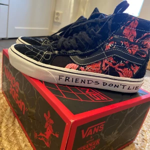 Svarta Vans Stranger Things sneakers - Unika svarta Vans sneakers i samarbete med Stranger Things. Skorna har ett coolt rött och svart mönster med texten 'Friends Don't Lie' på sulan. Perfekta för fans av serien som vill ha något speciellt i garderoben. Använd endast en gång då dem är för små. 