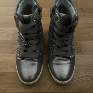 Sneakers - Skitsnygga glittriga sneakers med kilklack från Stuart Weitsman. Jätte mjuka inuti och sköna att gå i. Det står att dom är storlek 36, men är större i storleken, passar mig som har 37-38. Färgen skulle jag säga är en blandning mellan guld och grå. Dm för mer info🩷