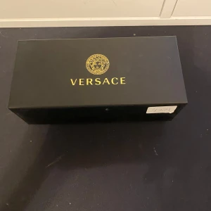 Svarta solglasögon från Versace - Snygga svarta solglasögon från Versace med en klassisk design. De kommer i ett elegant svart fodral med Versace-logotypen i guld. Perfekta för att ge en lyxig touch till din stil.