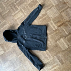 Svart hoodie från Nike - Säljer en svart hoodie från Nike med dragkedja och huva. Jackan har långa ärmar och är tillverkad i ett mjukt material. Perfekt för en avslappnad stil. Den är i storlek M (för barn) 137-147cm!