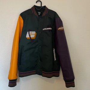 Bomberjacka - Bomberjacka med grön kropp och kontrasterande lila och gula ärmar. Jackan har broderade detaljer och knappar framtill. 