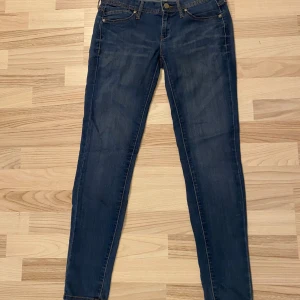 Blå jeans från Mango - Snygga blå jeans från Mango med en klassisk femficksdesign. De har en knapp och dragkedja framtill och är perfekta för en avslappnad stil. Märket 'Elektra' är broderat på insidan av linningen.