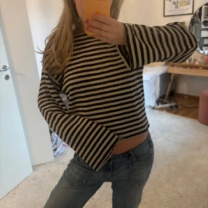 Randig stickad tröja - Säljer en randig stickad tröja i svart och beige. Tröjan har långa ärmar och en croppad passform. Perfekt för en avslappnad stil.