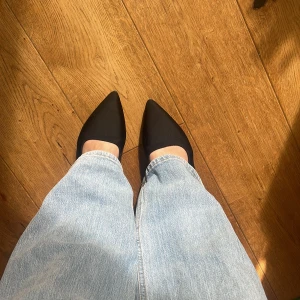 Svarta ballerinaskor med spetsig tå - Snygga svarta ballerinaskor med spetsig tå och öppen häl. Perfekta för en stilren look. De har en elegant design som passar till många olika outfits. Endast använda en gång!