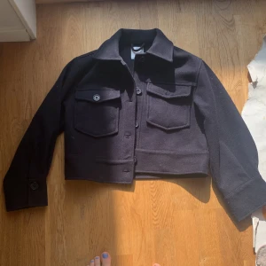 Marin blå jacka från Ginatricot 146/152  - Säljer en snygg svart jacka från Gina Tricot. Jackan har en croppad design med knappar framtill och två bröstfickor med lock. Perfekt för en stilren look.