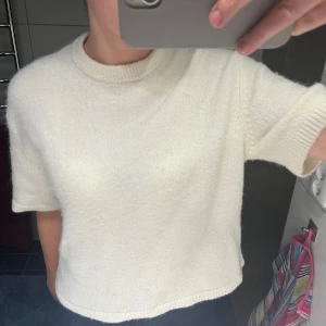 Vit stickad tröja - Säljer en stilren vit stickad tröja med korta ärmar. Perfekt för en avslappnad look. Tröjan har en rund halsringning och är gjord i ett mjukt material.