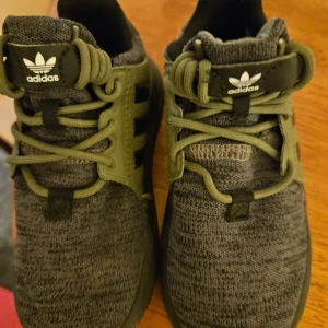 Grå och gröna sneakers från Adidas - Snygga grå och gröna sneakers från Adidas med klassisk design och bekväm passform. Skorna har en stickad ovandel och gröna snören som ger en sportig look. Perfekta för vardagsbruk.