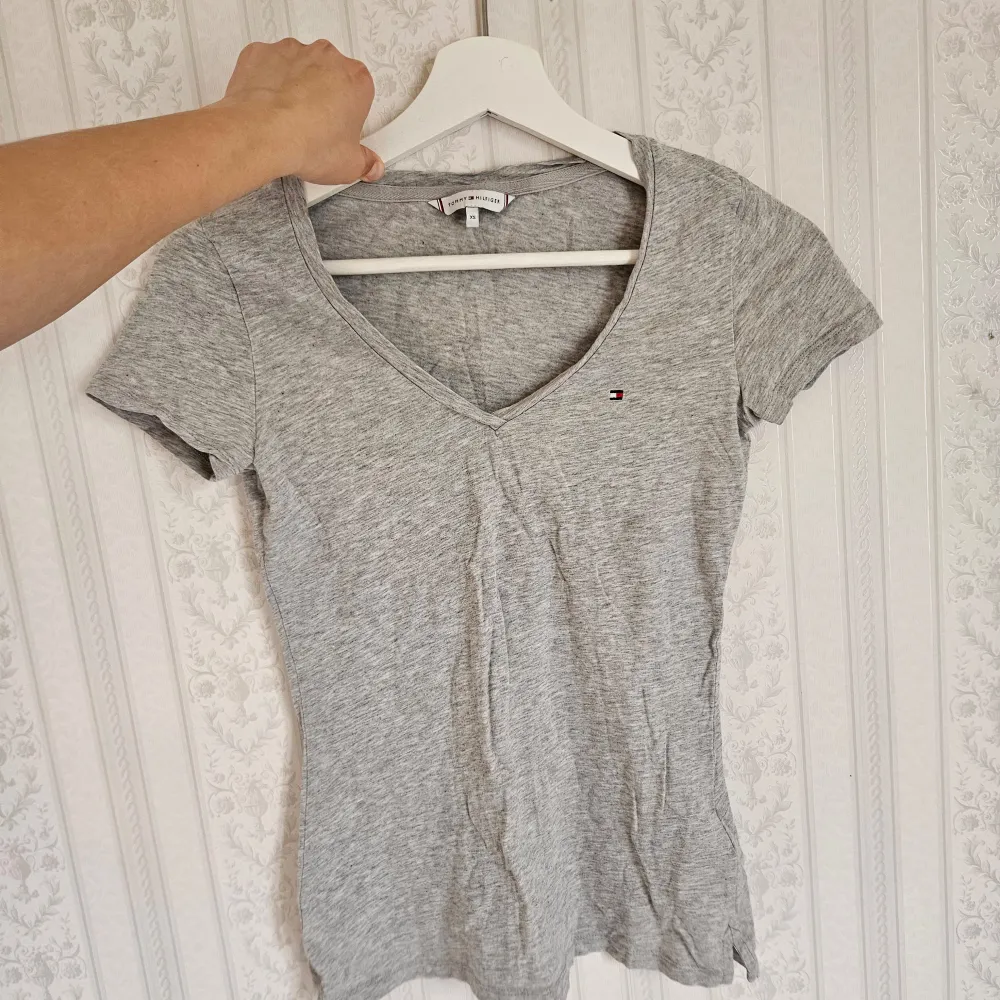 Säljer en stilren grå t-shirt från Tommy Hilfiger med v-ringning och korta ärmar. Lite skrynklig av att ha legat i garderoben - endast använd 2 gånger, mycket bra skick! 🩷. T-paidat.