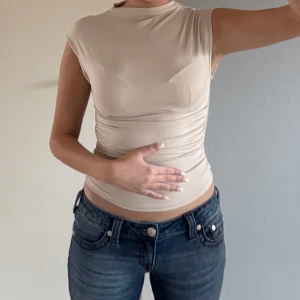 Beige topp från Gina Tricot - Säljer en stilren beige topp från Gina Tricot. Toppen har en tight passform och korta ärmar.