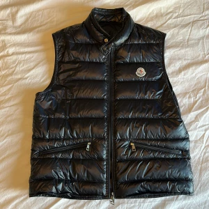 Moncler Gui Vest Navy - Säljer en Moncler Gui väst i färgen Navy. Finns ett litet flaw på insidan längst ned som är lagat (se bild). Annars är västen i bra skick.            Nypris: 9299kr                                                    Storlek 3 (medium)                                                           Köpt på NK Göteborg.                                            Kan skicka fler bilder om det önskas. 