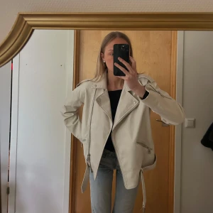 Vit skinnjacka - Snygg beige/vit skinnjacka med silvriga dragkedjor och bälte i midjan. Jackan har klassisk bikerstil med bred krage och långa ärmar. Perfekt för dig som vill ha en stilren och trendig look. Den känns upplevs lite  oversized!