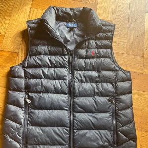 Blå dunväst från Polo Ralph Lauren - Stilren blå dunväst från Polo Ralph Lauren med ståkrage och dragkedja framtill. Västen har två fickor med dragkedja och klassisk röd logga broderad på bröstet. Perfekt för lager-på-lager och enkel att matcha. Den är i storlek XL i barnstorlek och passar dig som är runt 170. Västen har en liten slitning (se bild 5) som bara märks om man kollar nära. Priset kan diskuteras. Det är bara att höra av sig😁👍