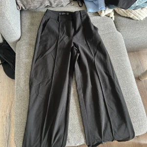 Svarta kostymbyxor från Amisu - Säljer ett par svarta kostymbyxor från Amisu i storlek 32. Byxorna har hög midja, vida ben och pressveck framtill. 