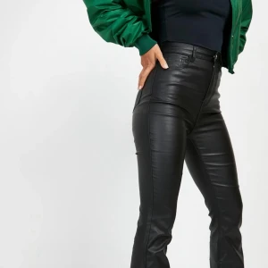 Svarta skinnbyxor med hög midja - Snygga svarta skinnbyxor med hög midja och klassisk femficksdesign. Byxorna har en slim passform och stängs med dragkedja och knapp.