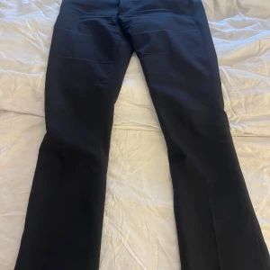 Svarta kostymbyxor från Bik Bok - Klassiska svarta kostymbyxor från Bik Bok med normal passform och raka ben. Byxorna har hällor för bälte och stängs med dragkedja och knapp. Perfekta till en stilren look. Lågmidjade med en slits längst ner💕
