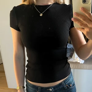Svart ribbad t-shirt - Säljer en svart ribbad t-shirt med tight passform och korta ärmar. T-shirten har rund halsringning och är tillverkad i ett stretchigt material.