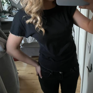 Svart t-shirt med pärldetaljer från Zara - Svart osymmetrisk t-shirt från Zara. På ena ärmen är ärmslutet dekorerat med pärlor som ger en snygg detalj. Tillverkad i mjuk bomull, perfekt för en unik, clean och stilren look🩷🩷