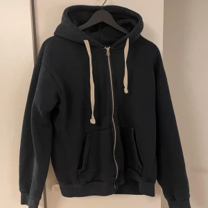 Zara hoodie - Säljer en svart hoodie från Zara i storlek M. Tröjan har dragkedja framtill, huva med vita snören och två stora fickor. Perfekt för en avslappnad stil och enkel att matcha med det mesta.