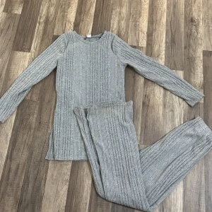 Ett grått stickat set  - Säljer en långärmad, grå stickad tröja med ribbat mönster och rund hals. Tröjan har en längre passform med slitsar i sidorna, finns även matchade byxor till.