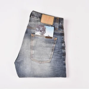 Blå slim raka jeansbyxor med knappar - Säljer ett par helt nya klassiska blå jeansbyxor från Nudie Jeans Co med raka ben och knappar i gylfen. Jeansen har en snygg tvätt med ljusare partier och fem fickor. Perfekta för dig som gillar en tidlös stil. Dock passade den tyvärr inte mig. Stolek 30:34