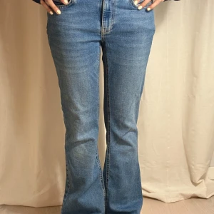 Blå bootcut jeans - Säljer ett par klassiska blå bootcut jeans med medel hög midja. Jeansen har fram fickor, dragkedja och knapp framtill samt utsvängda ben. Perfekta för dig som gillar en retroinspirerad look.
