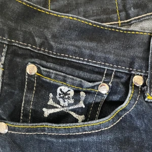 Zoo York jeans med dödskalle och pistol-tryck - Unika mörkblå jeans från Zoo York med coola tryck av dödskalle, korslagda benknotor och pistol. Gula kontrastsömmar och detaljerade bakfickor. Perfekta för dig som vill sticka ut med streetwear-stil. Jag går me på lägre om de är realistiskt pris!