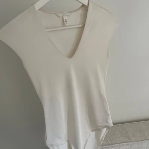 Vit v-ringad bodysuit  - Säljer en enkel och stilren vit bodysuit från H&M med v-ringning. Mjukt material som sitter skönt mot kroppen.