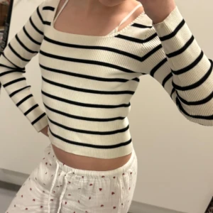 Vit och svart randig croppad tröja - Säljer en vit ribbad tröja med svarta horisontella ränder. Tröjan är croppad, har lång ärm och en fyrkantig ringning. Perfekt för dig som gillar en enkel men stilren look.