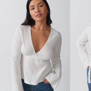 Vit omlottopp med knytband - Säljer en stilren vit omlottopp med djup v-ringning och långa ärmar. Toppen har knytband i midjan som ger en snygg siluett. Perfekt att matcha med jeans eller kjol för en trendig look.