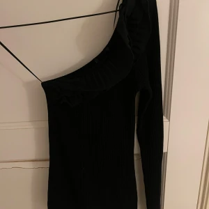 Svart oneshoulder topp med volang - Säljer en svart oneshoulder topp med lång ärm och volangdetalj längs halsringningen. Toppen har en tight passform, toppen är oanvänd. Från Zara. Priset går att diskutera. 