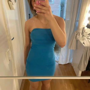 Blå axelbandslös tight klänning - Säljer en blå axelbandslös klänning med tight passform. Klänningen är kort och har en enkel, stilren design utan mönster eller extra detaljer. Perfekt för dig som gillar minimalistisk stil och vill sticka ut med färg.