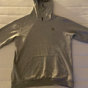 Grå hoodie från Lyle & Scott - Säljer en klassisk grå hoodie från Lyle & Scott med gul logga på bröstet. Tröjan har huva och en stor magficka framtill. Den är knappt använd och har storlek 15/16 år! Ifall det är några frågor är det bara att skicka!