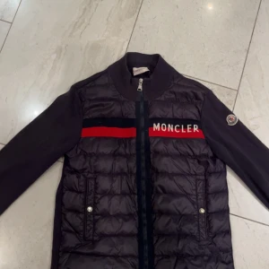 Svart cardigan från Moncler - Säljer en svart moncler cardigan med rött sträck och moncler logga på. Jag säljer jackan eftersom den inte passar mig🥰☺️