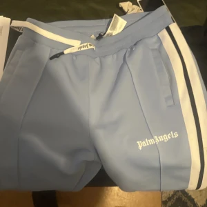 Ljusblåa byxor  från Palm Angels ,passar m XL - Snygga ljusblåa träningsbyxor från Palm Angels. Byxorna har raka ben och elastisk midja för skön passform. 