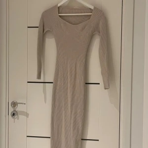 Beige ribbad långklänning - Säljer en beige ribbad långklänning med lång ärm och v-ringad halsringning. Klänningen har en figurnära passform och är tillverkad i ett stretchigt stickat material. Perfekt för dig som gillar en enkel men stilren look. Knappt använd!
