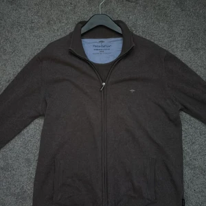 Brun ziptröja från Fynch-Hatton - Säljer en brun ziptröja från Fynch-Hatton i mjuk bomull. Tröjan har hög krage, hel dragkedja framtill och två fickor. Perfekt för lager-på-lager och enkel att matcha med det mesta.